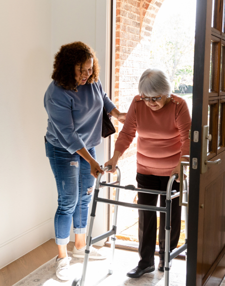 Support worker assisting an older adult with a walker at the doorway